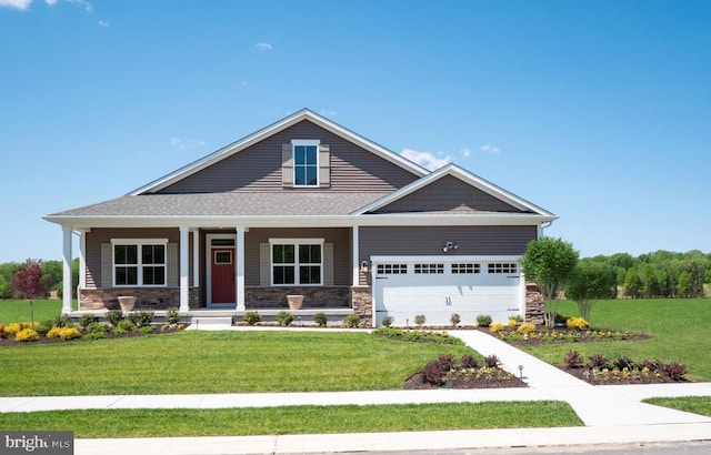 craftsman house featuring stone siding, covered porch, an attached garage, and a front yard