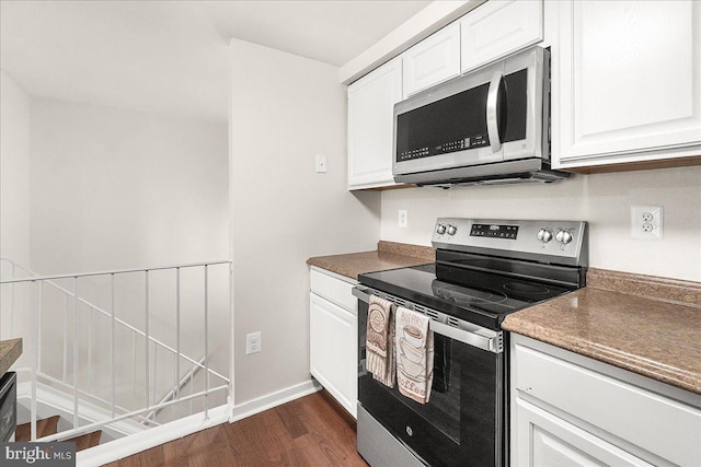 kitchen with dark countertops, dark wood finished floors, white cabinetry, appliances with stainless steel finishes, and baseboards