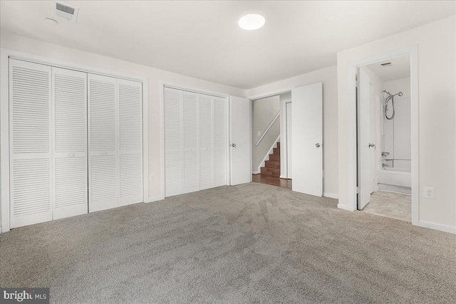 unfurnished bedroom with carpet flooring, ensuite bath, visible vents, and multiple closets