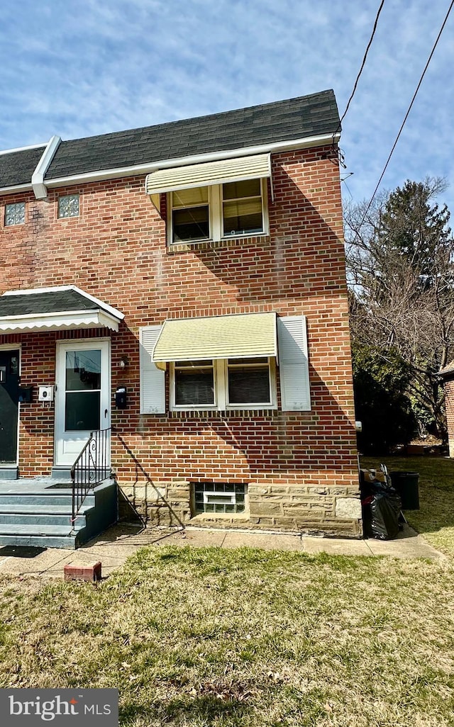 view of front facade featuring brick siding, a shingled roof, and a front lawn