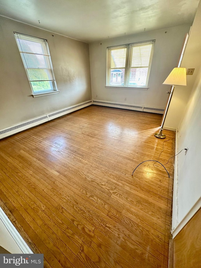 spare room featuring baseboard heating, plenty of natural light, and wood finished floors