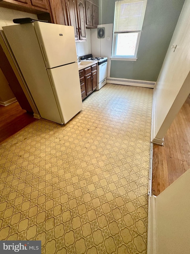 kitchen with a baseboard heating unit, baseboards, light floors, light countertops, and white appliances