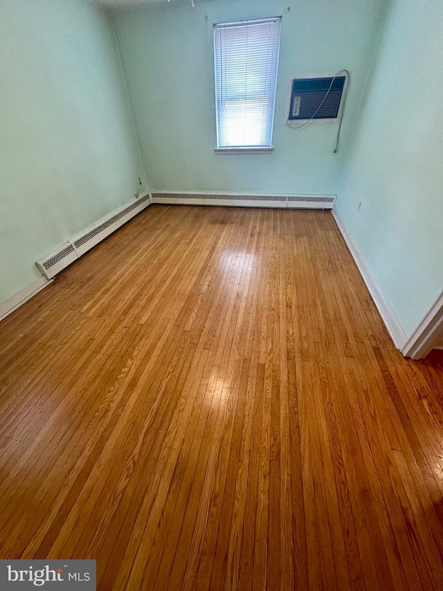 empty room with a baseboard heating unit, wood-type flooring, a wall mounted air conditioner, and a baseboard radiator