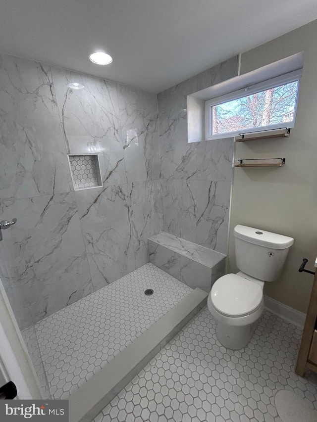 bathroom featuring tiled shower, toilet, and baseboards