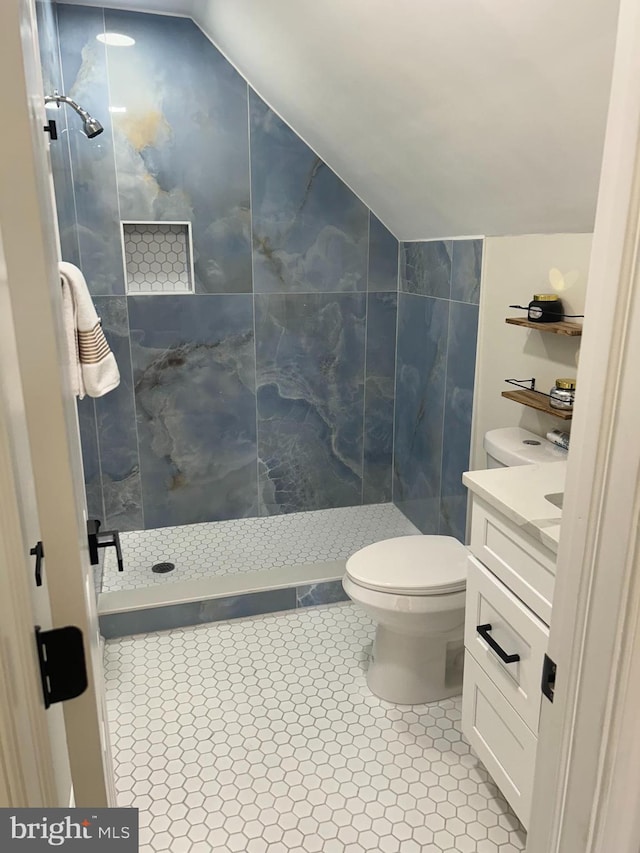 bathroom featuring tile patterned flooring, lofted ceiling, toilet, and tiled shower