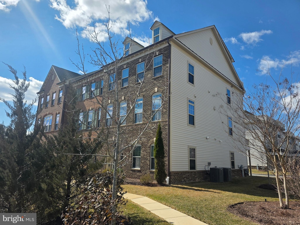 view of side of home featuring brick siding, central AC, and a yard