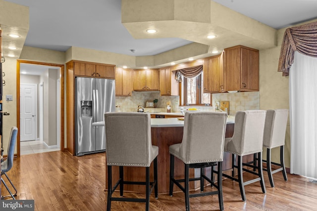 kitchen with stainless steel fridge, a peninsula, wood finished floors, and light countertops