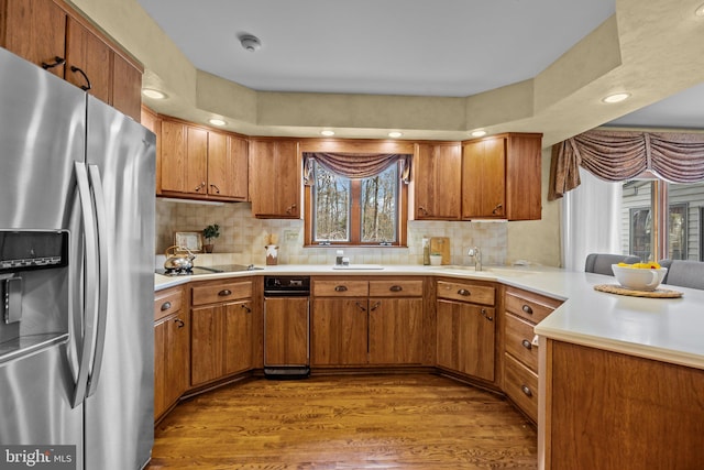 kitchen featuring brown cabinets, stainless steel refrigerator with ice dispenser, wood finished floors, a peninsula, and light countertops