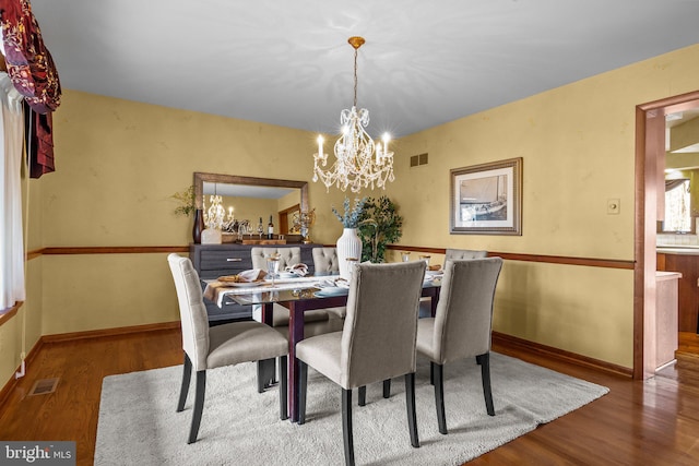 dining area featuring a chandelier, visible vents, baseboards, and wood finished floors