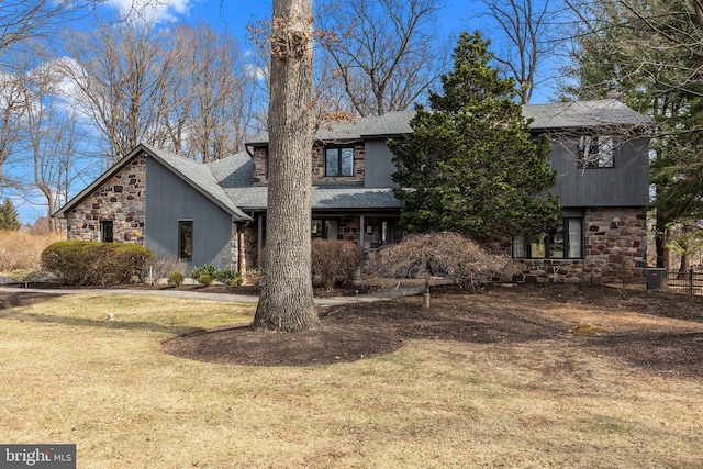 view of front of house with stone siding, a shingled roof, and a front yard