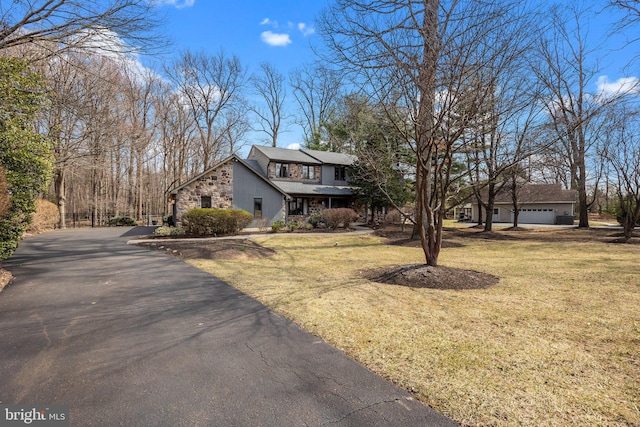 view of front facade featuring aphalt driveway, stone siding, a garage, and a front yard