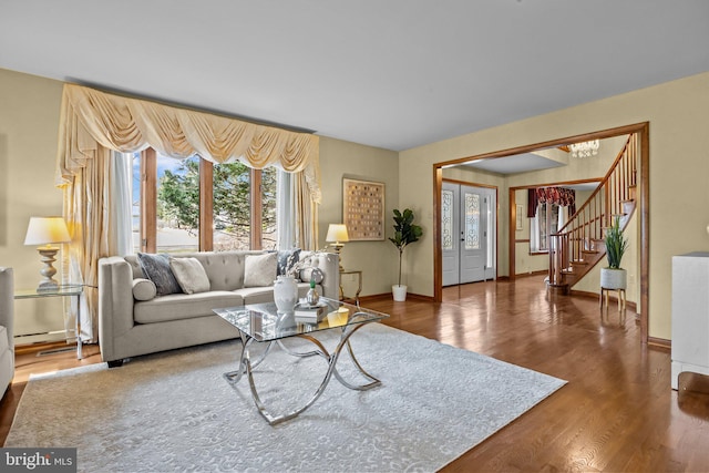 living room featuring a chandelier, stairway, baseboards, and wood finished floors