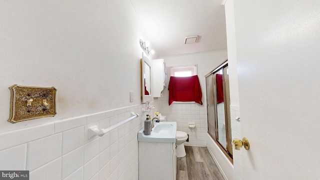 full bath featuring toilet, wood finished floors, tile walls, wainscoting, and vanity