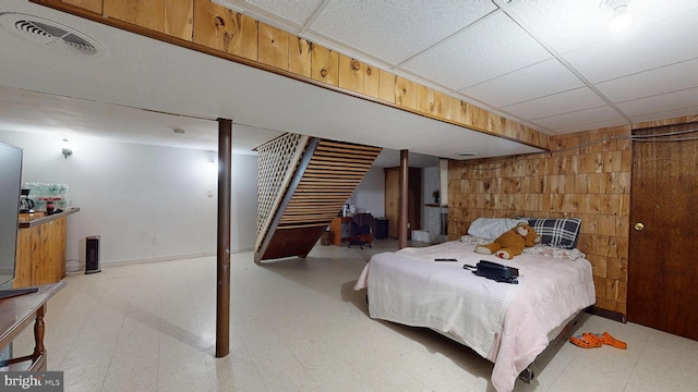 bedroom featuring a drop ceiling, visible vents, light floors, and wood walls