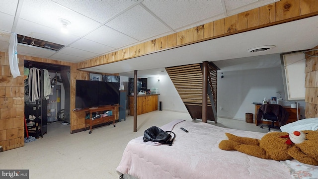 bedroom featuring water heater, visible vents, wooden walls, and a drop ceiling