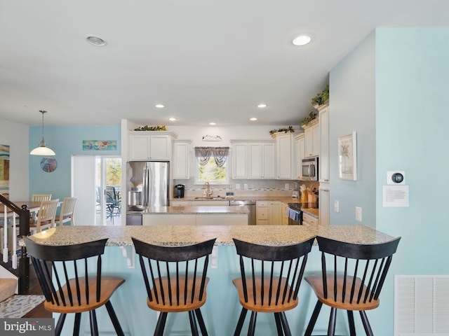 kitchen with visible vents, a kitchen island, a sink, appliances with stainless steel finishes, and a kitchen bar