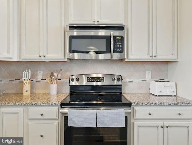 kitchen featuring decorative backsplash, light stone countertops, white cabinetry, and appliances with stainless steel finishes