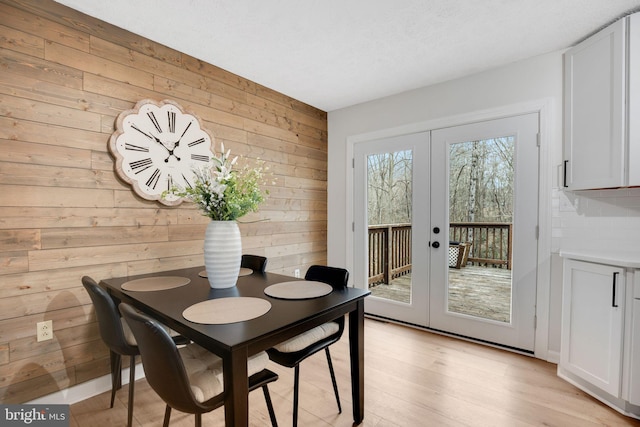 dining area with light wood-type flooring, french doors, and wooden walls