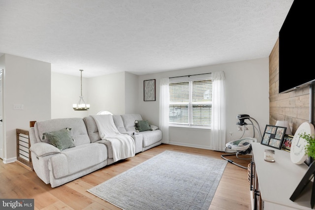 living room with a textured ceiling, light wood-style flooring, baseboards, and a chandelier