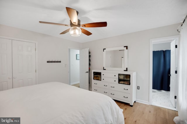 bedroom featuring a ceiling fan, ensuite bath, a closet, light wood-style floors, and baseboards