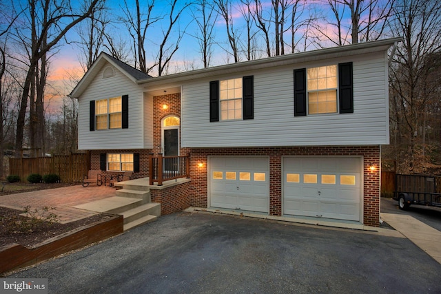 split foyer home featuring aphalt driveway, an attached garage, brick siding, and fence