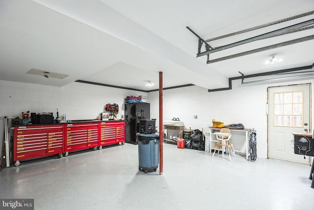 garage with a workshop area, black fridge, and concrete block wall