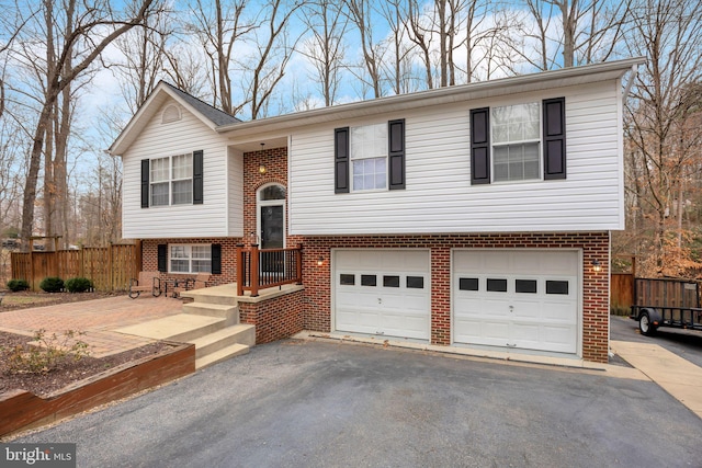 raised ranch featuring brick siding, aphalt driveway, a garage, and fence