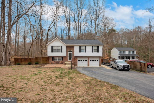 raised ranch with an attached garage, fence, brick siding, and driveway