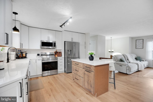 kitchen featuring open floor plan, appliances with stainless steel finishes, a breakfast bar area, and light wood-style floors