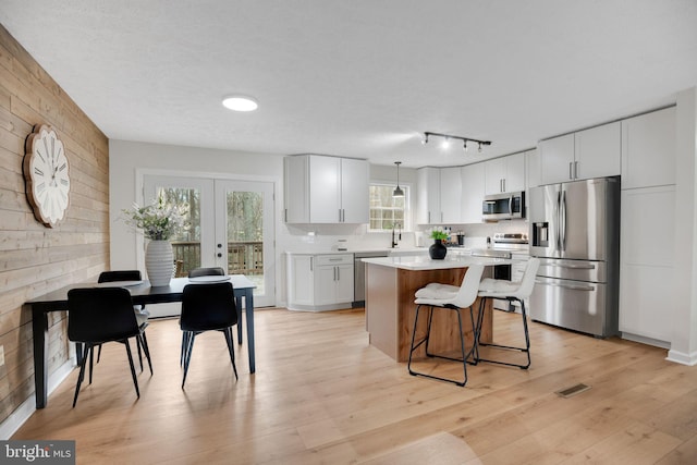 kitchen with light wood-style flooring, light countertops, wood walls, appliances with stainless steel finishes, and a center island