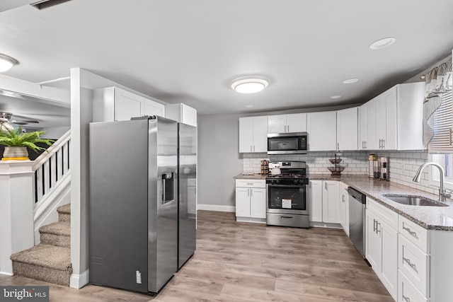 kitchen with tasteful backsplash, light wood-type flooring, light stone counters, appliances with stainless steel finishes, and a sink