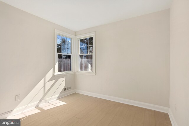 empty room featuring wood finished floors, visible vents, and baseboards