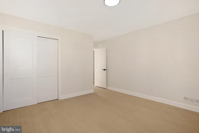 unfurnished bedroom with a closet, baseboards, visible vents, and light wood finished floors