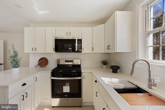 kitchen with decorative backsplash, a peninsula, white cabinets, stainless steel appliances, and a sink