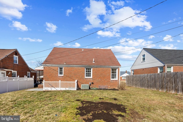 rear view of property featuring central air condition unit, fence private yard, brick siding, and a lawn