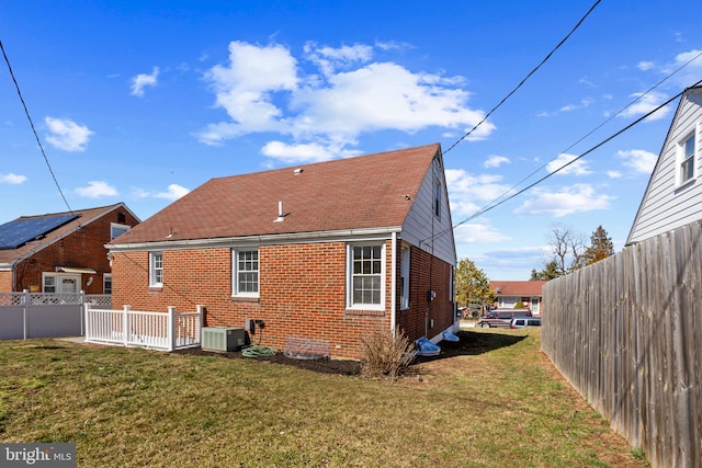 rear view of property featuring brick siding, cooling unit, a yard, and fence