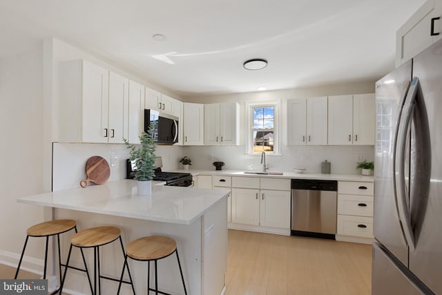 kitchen featuring a peninsula, a sink, appliances with stainless steel finishes, a kitchen breakfast bar, and backsplash