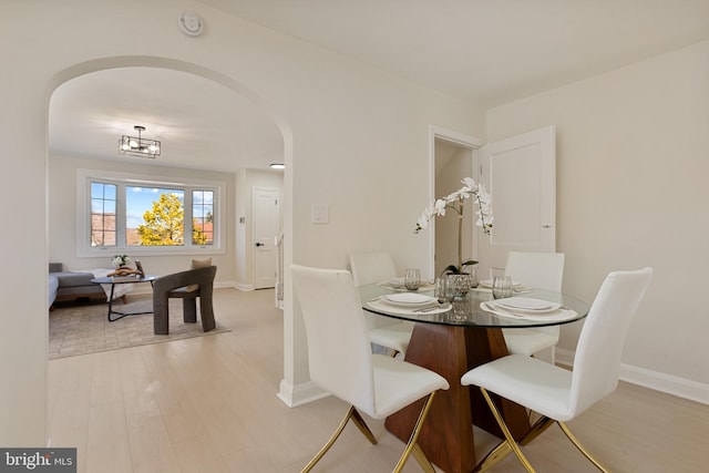 dining room with arched walkways, light wood-style flooring, and baseboards