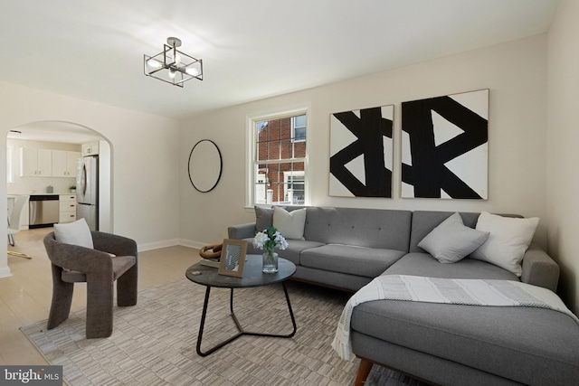 living room with baseboards, arched walkways, a notable chandelier, and light wood finished floors