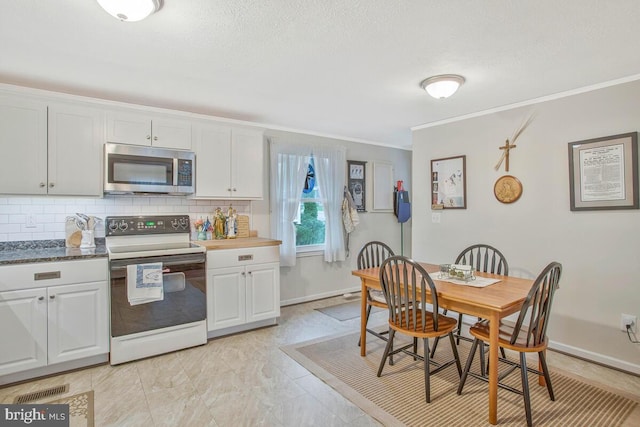 3719 3rd St, North Beach, MD 20714 - kitchen with stainless steel microwave, range with electric cooktop, crown molding, tasteful backsplash, and white cabinets