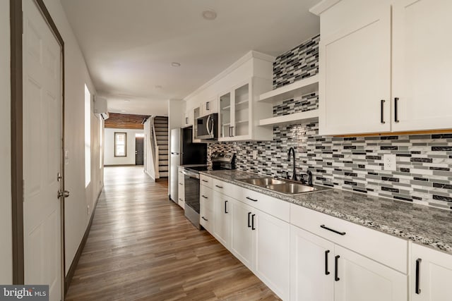 kitchen with a sink, open shelves, wood finished floors, stainless steel appliances, and decorative backsplash