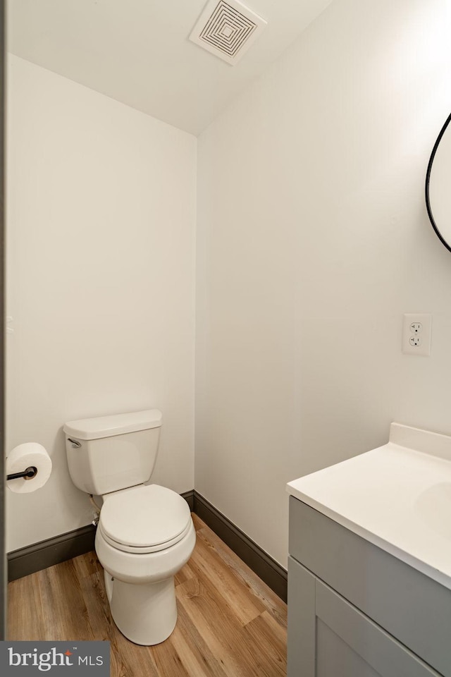 half bath with visible vents, toilet, vanity, and wood finished floors