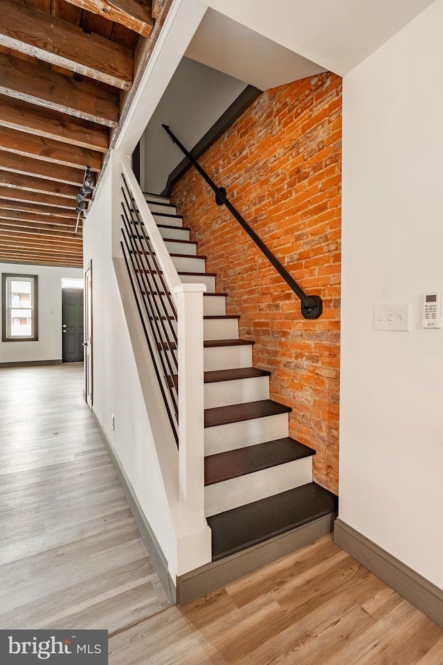 stairs with wood finished floors, baseboards, and brick wall