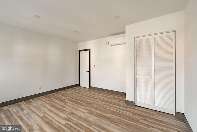 unfurnished bedroom with an AC wall unit, baseboards, light wood-type flooring, and a closet