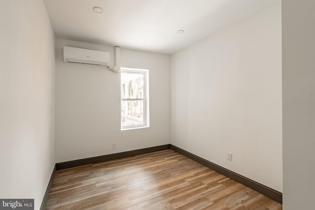 unfurnished room with a wall mounted air conditioner, light wood-type flooring, and baseboards