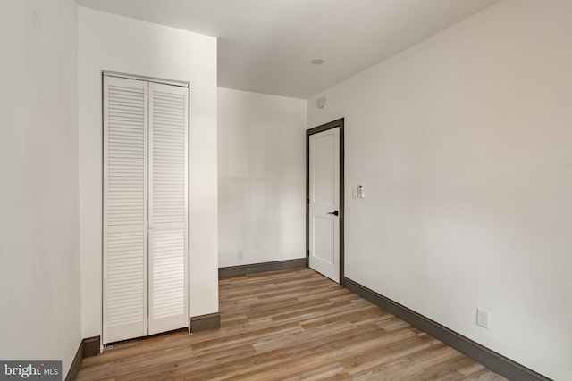 unfurnished bedroom featuring a closet, light wood-type flooring, and baseboards