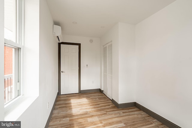 unfurnished room featuring light wood-type flooring, a wall mounted AC, and baseboards