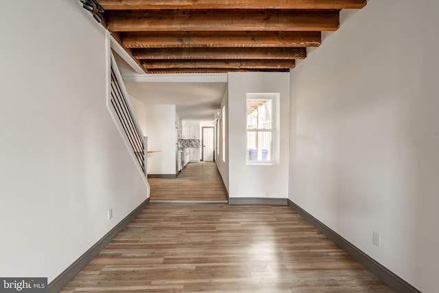 hallway with beamed ceiling, baseboards, wood finished floors, and stairway