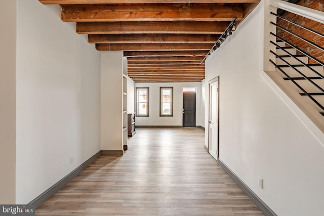 corridor with baseboards, beam ceiling, stairs, and light wood finished floors