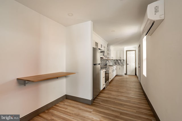 kitchen with a wall unit AC, decorative backsplash, light wood-style flooring, appliances with stainless steel finishes, and white cabinetry